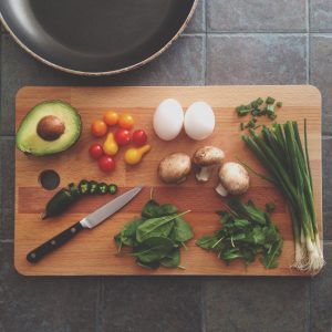 Raw healthy vegetables cut up on a wooden chopping board with a knife beside them