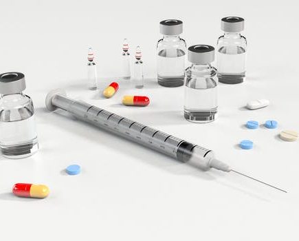 A syringe with vials of liquid chemicals and pain killer tablets scattered on a table to be used for non-surgical facelift Glasgow