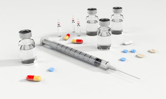 A syringe with vials of liquid chemicals and pain killer tablets scattered on a table to be used for non-surgical facelift Glasgow