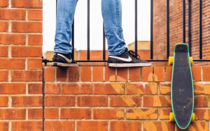 View of a boy climbing on a wall with his skateboard that he uses for exercise